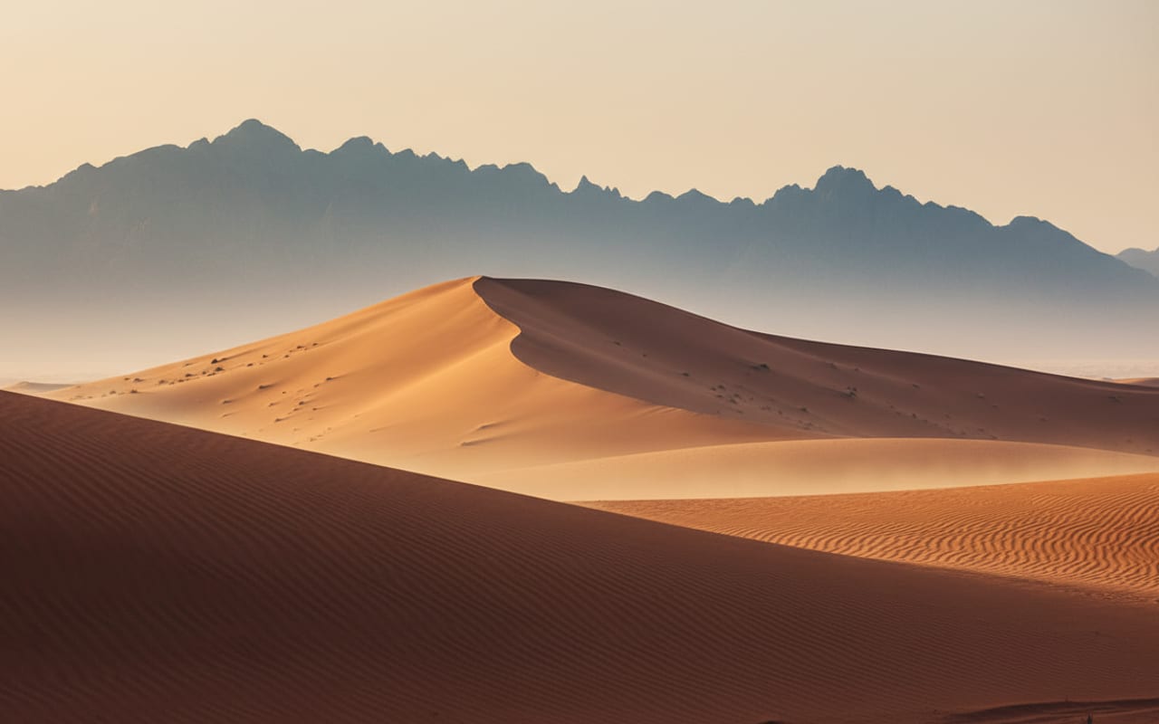 Three layered desert geographies — Dubai red dunes, Abu Dhabi golden Liwa ridge, Ras Al Khaimah Hajar mountain silhouette